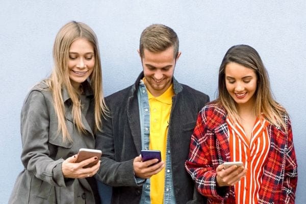 three people standing next to each other looking at their cell phones